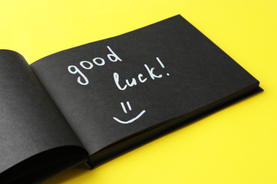 Photo of Notebook with phrase GOOD LUCK and funny face on yellow background, closeup