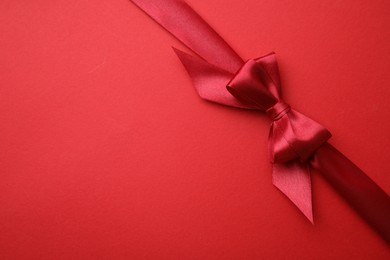 Photo of Bright satin ribbon with bow on red background, top view. Space for text