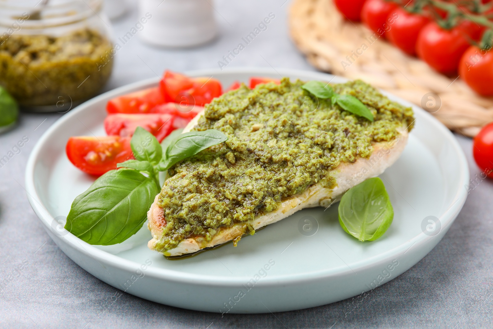 Photo of Delicious chicken breast with pesto sauce and basil on light gray table, closeup