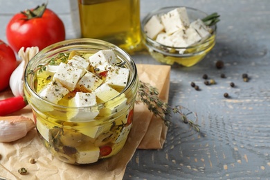 Composition with pickled feta cheese in jar on grey wooden table, space for text