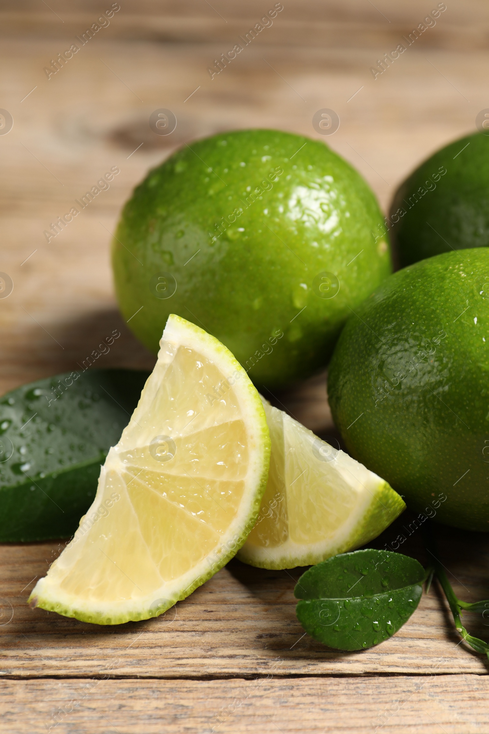 Photo of Fresh limes and green leaves with water drops on wooden table, closeup