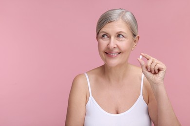 Photo of Beautiful woman with vitamin pill on pink background, space for text