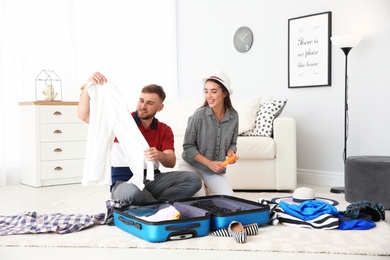 Photo of Young couple packing suitcase for summer journey at home