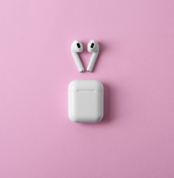 Photo of Modern wireless earphones and charging case on pink background, flat lay