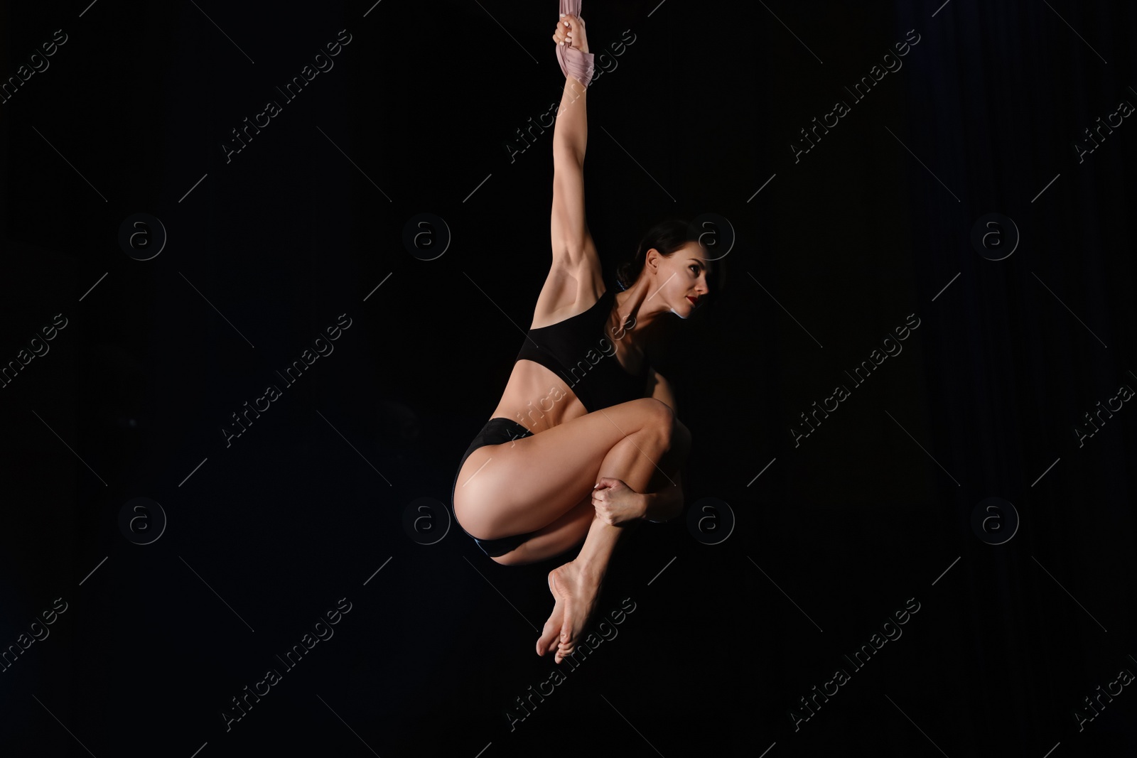 Photo of Young woman performing acrobatic element on aerial silk indoors