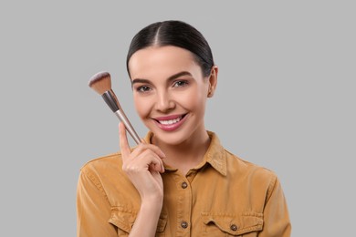 Happy woman with makeup brush on light grey background