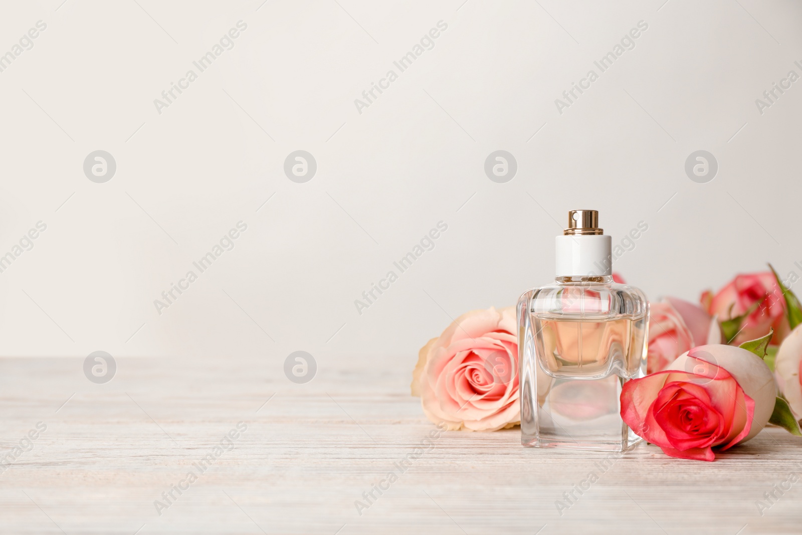 Photo of Bottle of perfume and flowers on table against light background