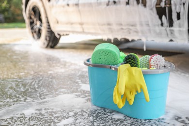 Photo of Car cleaning supplies and auto covered with foam outdoors, space for text