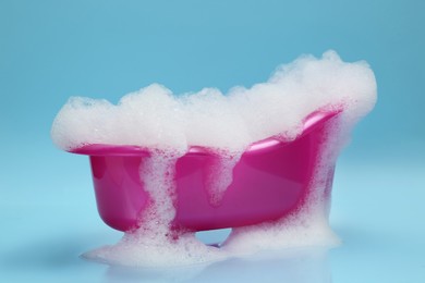 Photo of Toy bathtub overflowing with foam on light blue background
