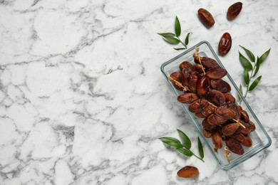 Tasty sweet dried dates and green leaves on white marble table, flat lay. Space for text