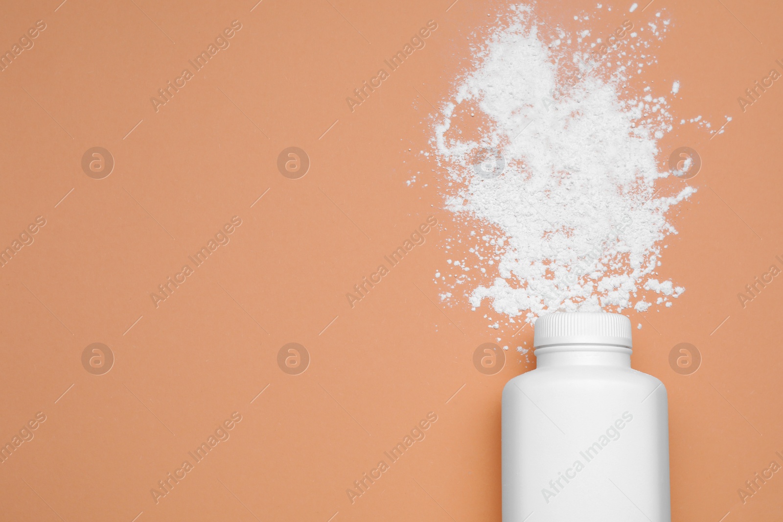 Photo of Bottle and scattered dusting powder on pale coral background, top view with space for text. Baby cosmetic product