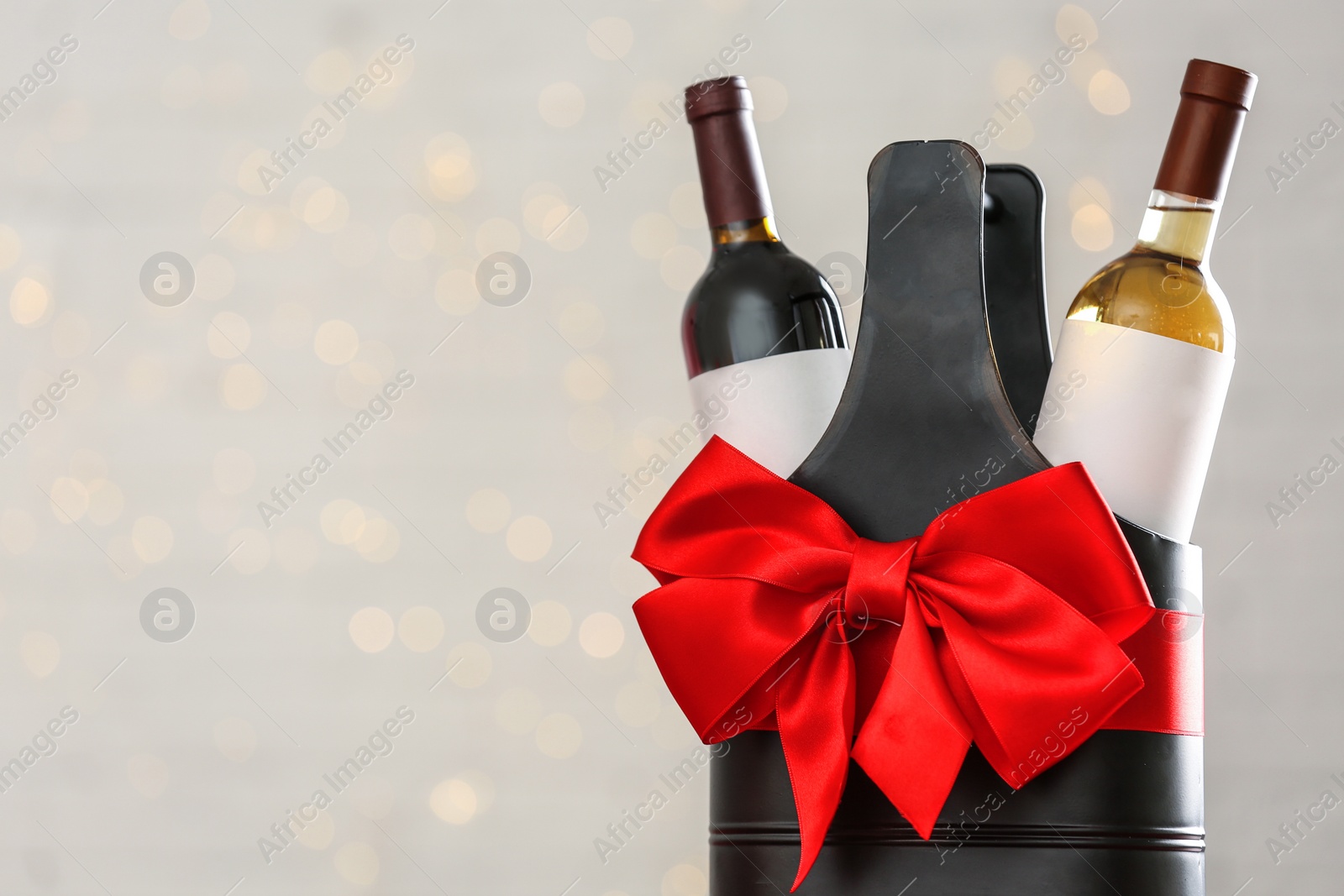 Photo of Bottles of wine in holder with bow against blurred lights. Space for text