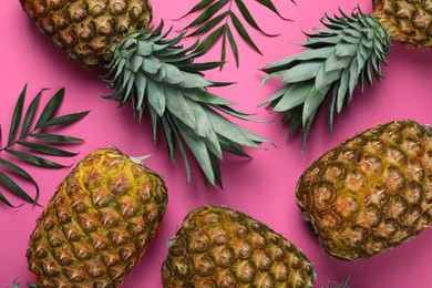 Photo of Whole ripe pineapples and green leaves on pink background, flat lay