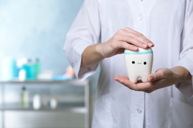 Photo of Dentist holding model of tooth with cute face in clinic, closeup view. Space for text