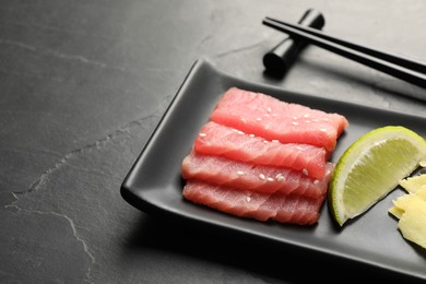 Photo of Tasty sashimi (pieces of fresh raw tuna) and lime wedge on black table, closeup