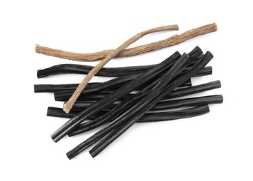 Tasty black candies and dried sticks of liquorice root on white background, top view