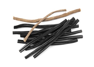 Photo of Tasty black candies and dried sticks of liquorice root on white background, top view