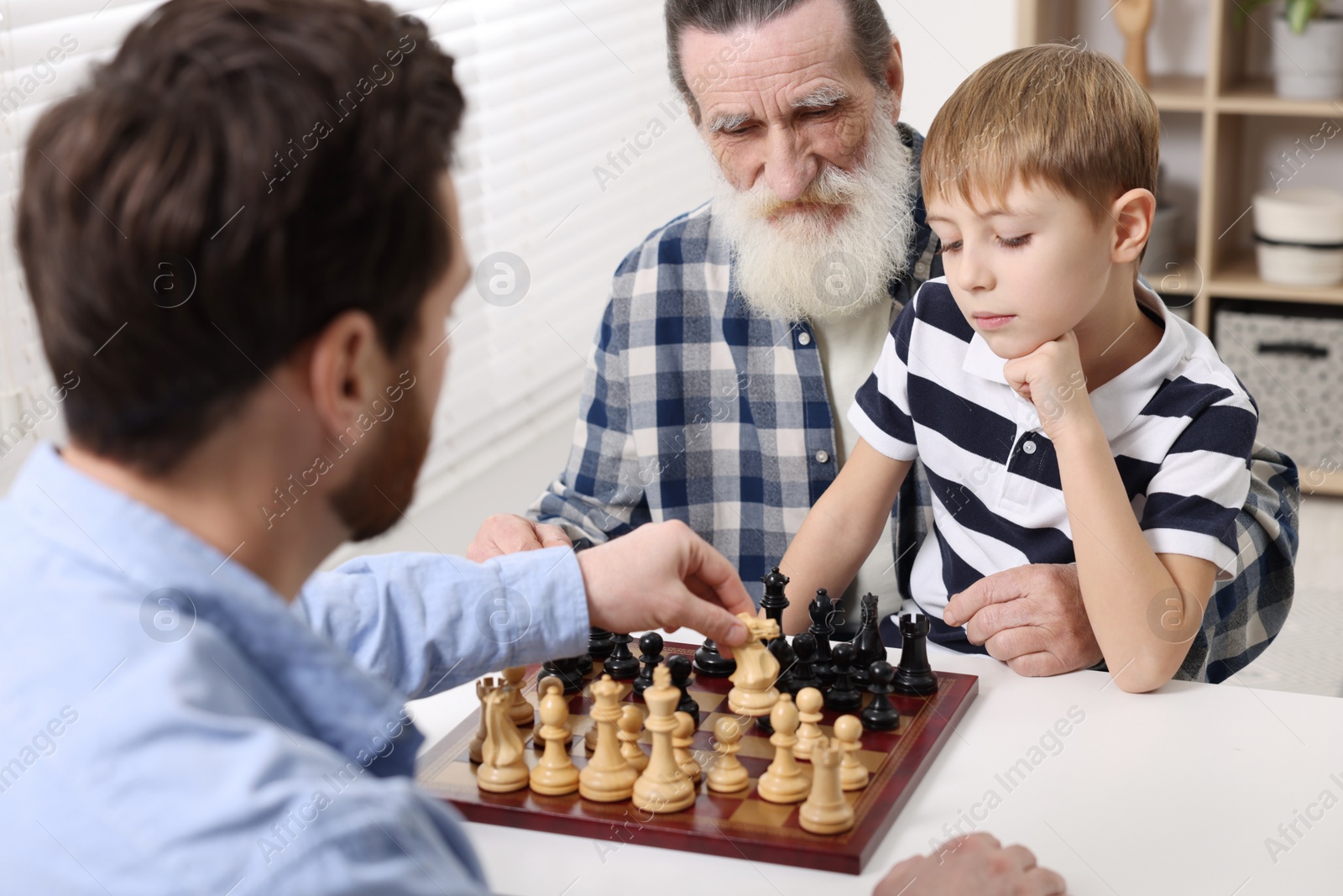 Photo of Family playing chess together at table in room