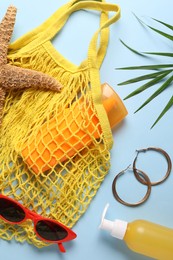 String bag, different beach accessories and palm leaf on light blue background, flat lay