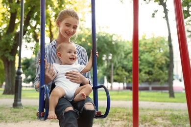 Teen nanny with cute little baby on swing outdoors. Space for text