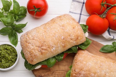 Delicious Caprese sandwiches with mozzarella, tomatoes, basil and pesto sauce on white wooden table, flat lay