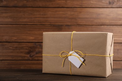 Photo of Parcel wrapped in kraft paper with tag on wooden table, space for text