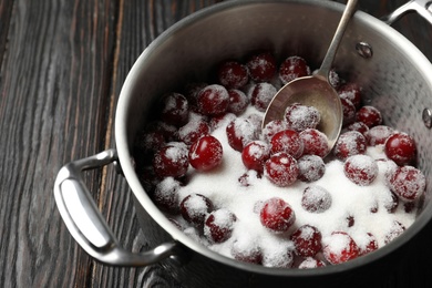 Photo of Pot with cherries and sugar on black wooden table, closeup. Making of delicious jam