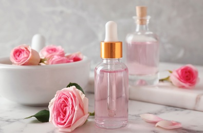 Photo of Bottle of essential oil and rose on marble table