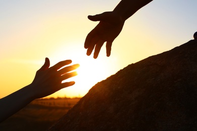 Photo of Hiker helping friend outdoors at sunset. Help and support concept