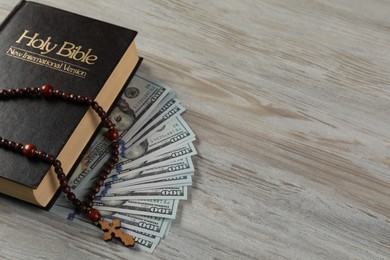 Photo of Holy Bible, cross and money on wooden table, closeup. Space for text