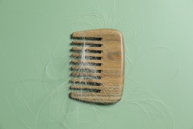 Photo of Comb with lost hair on green background, top view