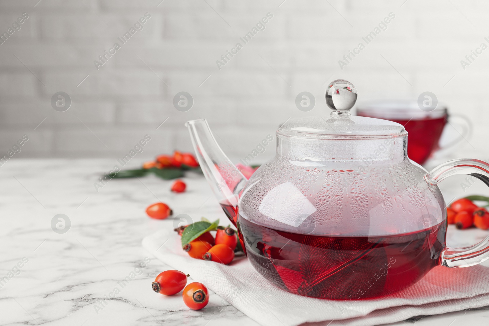 Photo of Fresh rose hip tea and berries on white marble table. Space for text