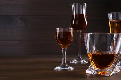 Different delicious liqueurs in glasses on wooden table. Space for text