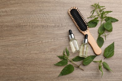 Photo of Stinging nettle, extract and brush on wooden background, flat lay with space for text. Natural hair care