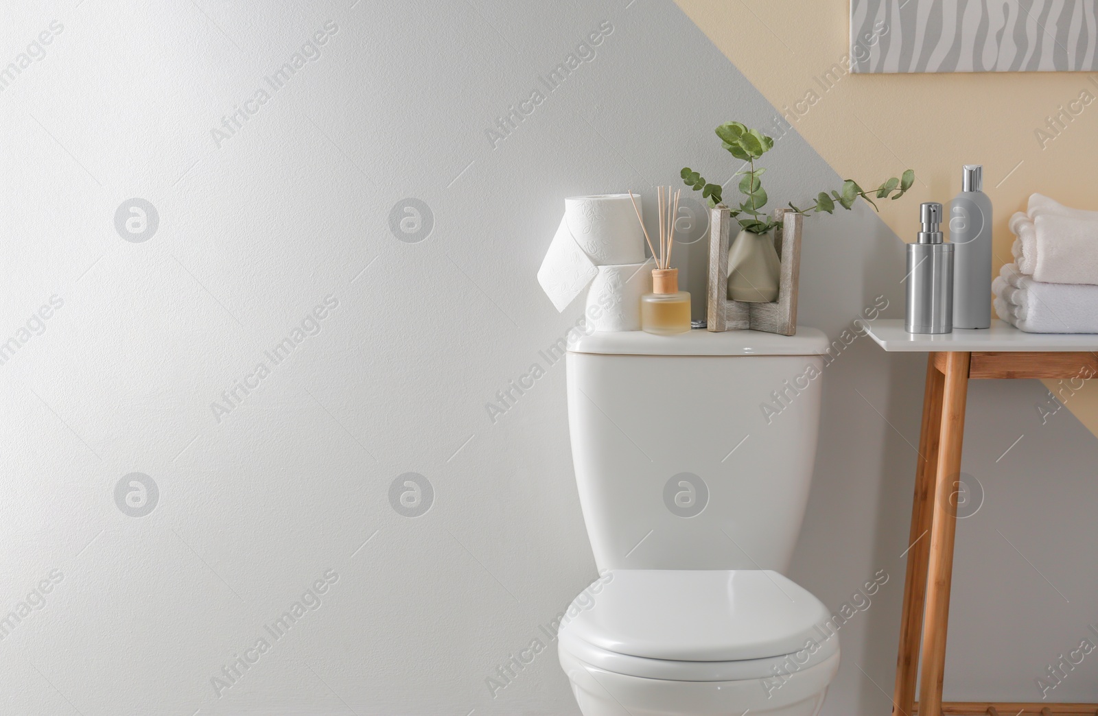 Photo of Table and toilet bowl with decor elements and necessities near color wall. Bathroom interior