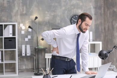 Young man suffering from back pain in office