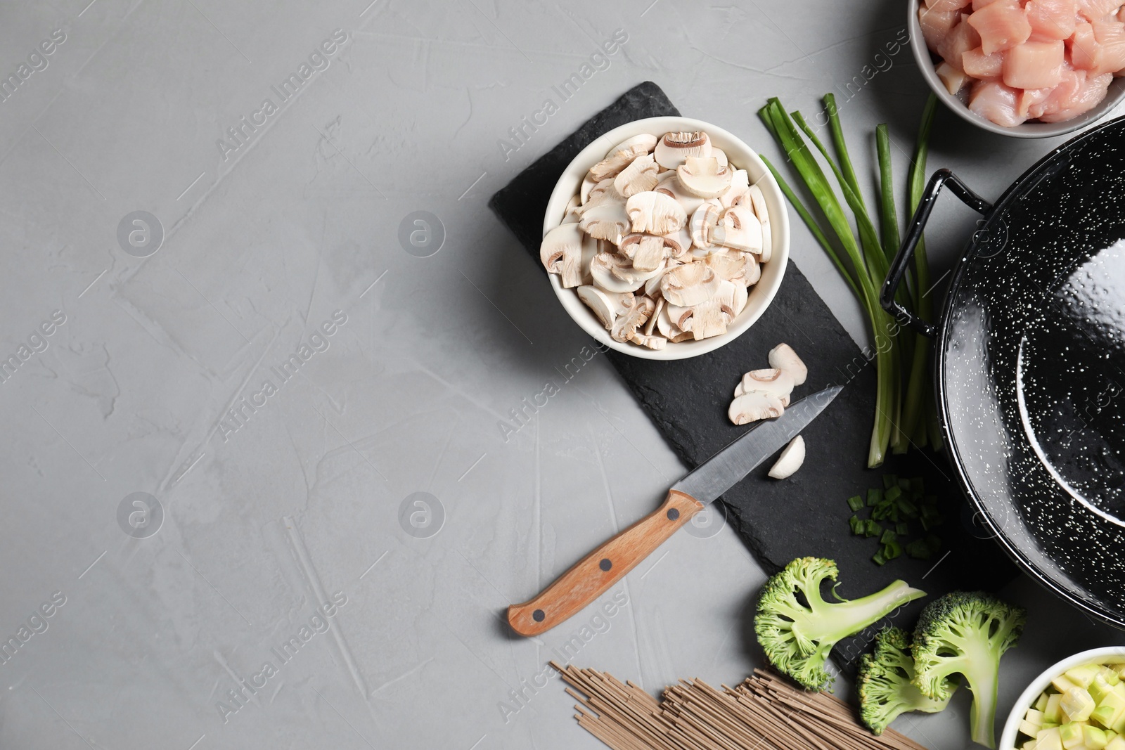 Photo of Wok pan, noodles, chicken and other products on light grey table, flat lay. Space for text