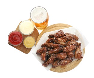 Photo of Wooden board with tasty roasted chicken wings, glass of beer and sauces isolated on white, top view