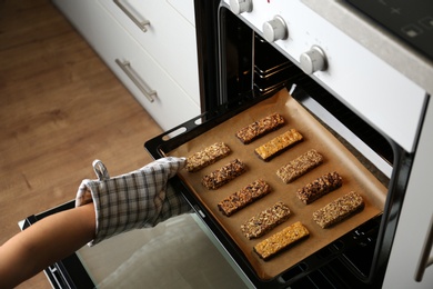 Woman taking delicious healthy granola bars from oven, closeup