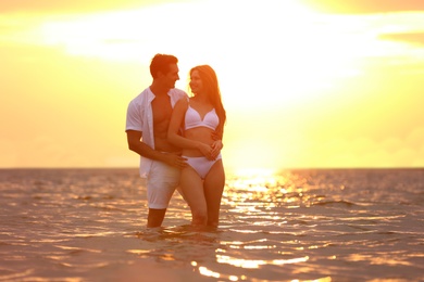 Happy young couple spending time together on sea beach at sunset