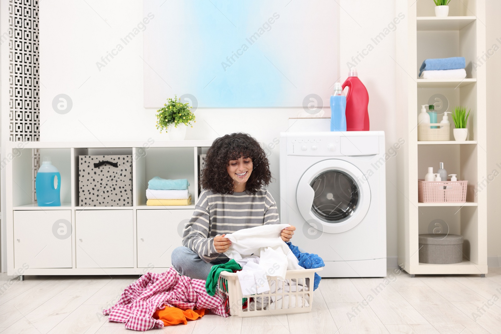 Photo of Happy woman with laundry near washing machine indoors