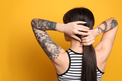 Photo of Beautiful woman with tattoos on arms against yellow background, back view