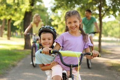 Photo of Happy siblings and their parents riding bicycles in park