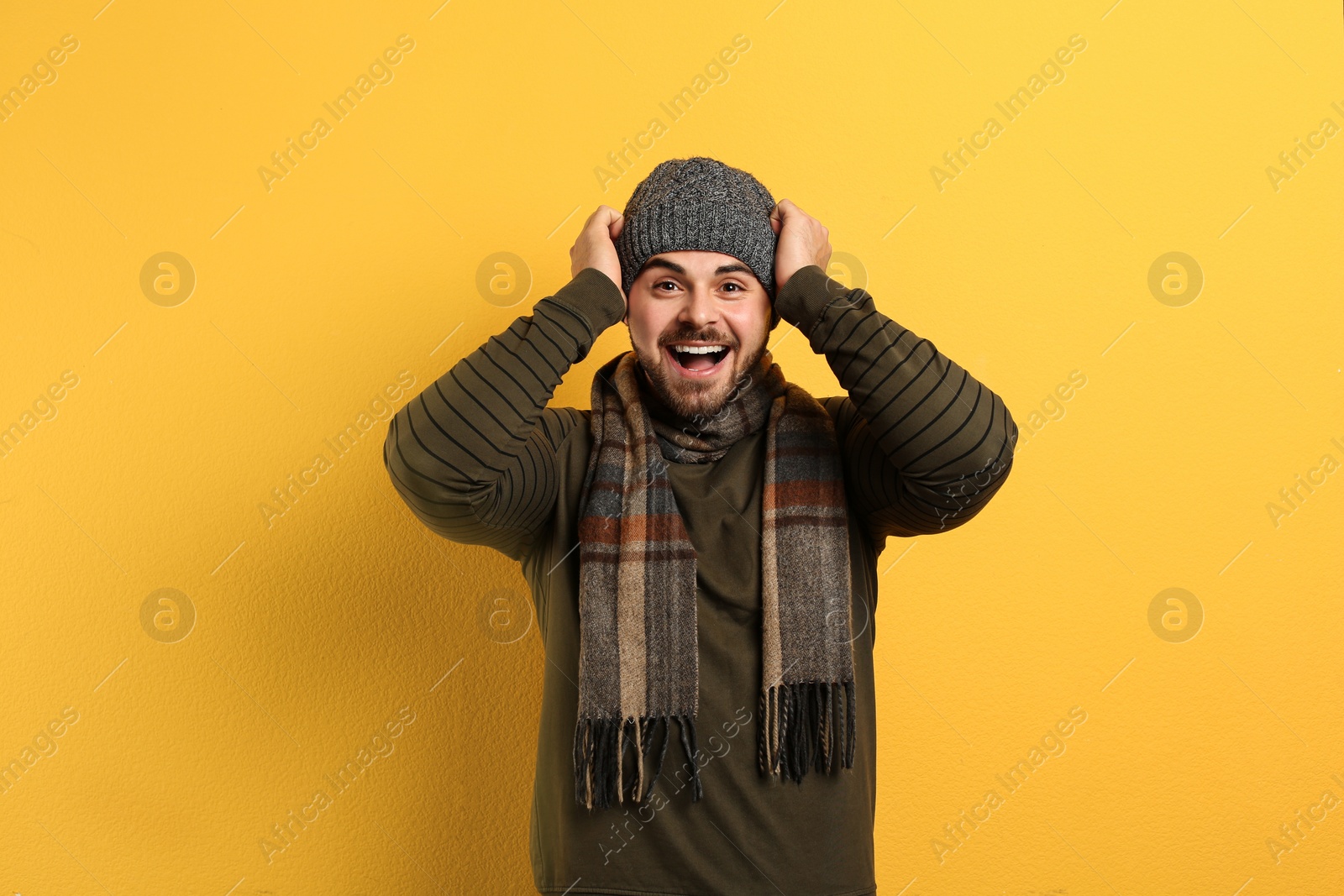 Photo of Happy young man in warm clothes on yellow background. Winter vacation