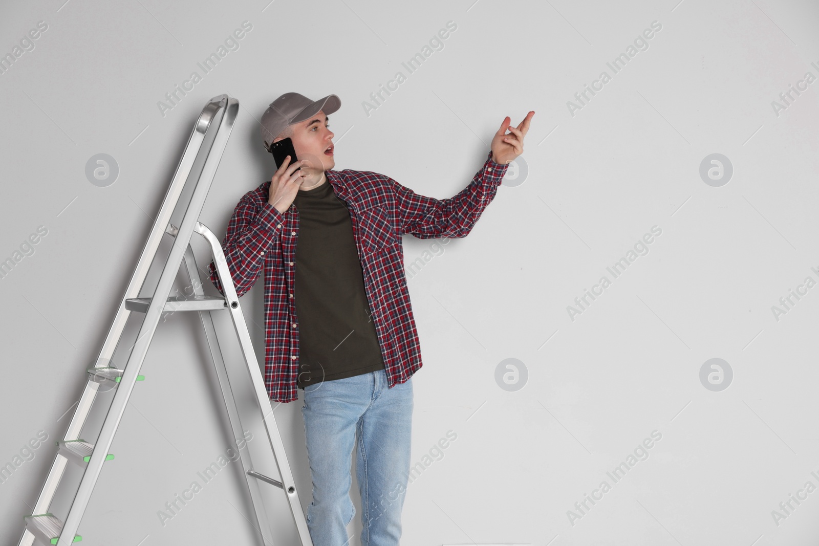 Photo of Emotional handyman talking on phone near stepladder in room