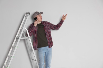 Emotional handyman talking on phone near stepladder in room
