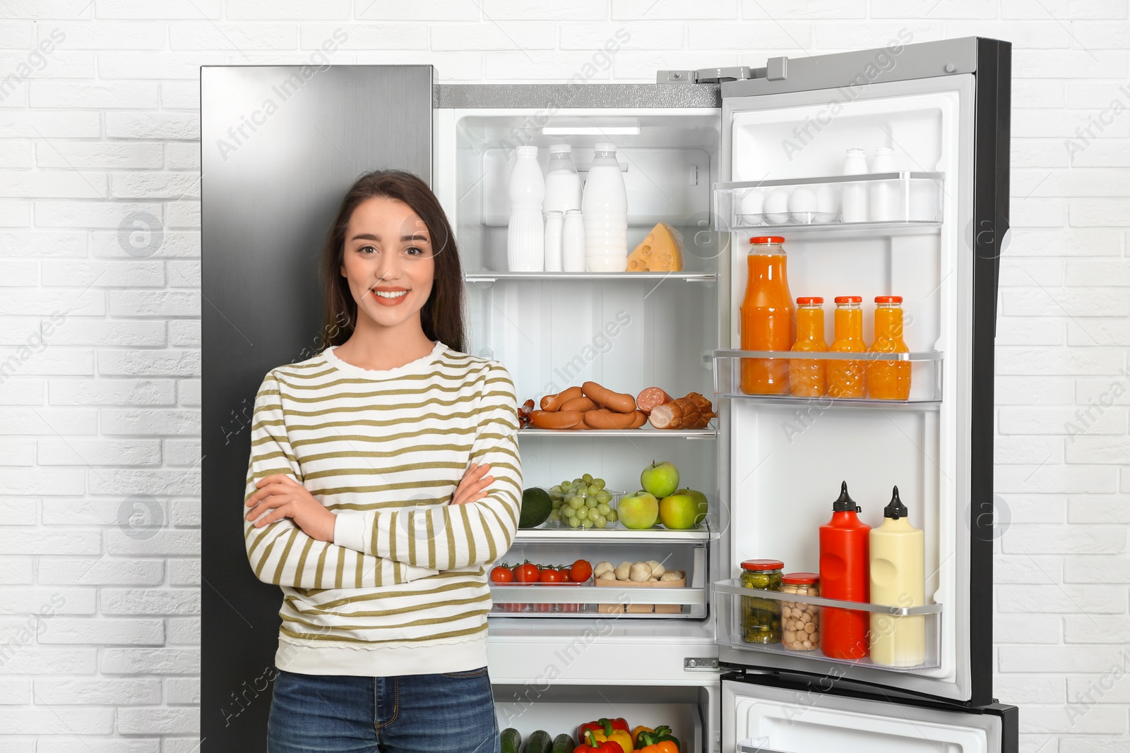 Photo of Happy young woman near open refrigerator indoors