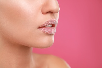 Young woman with sugar scrub on lips against pink background, closeup