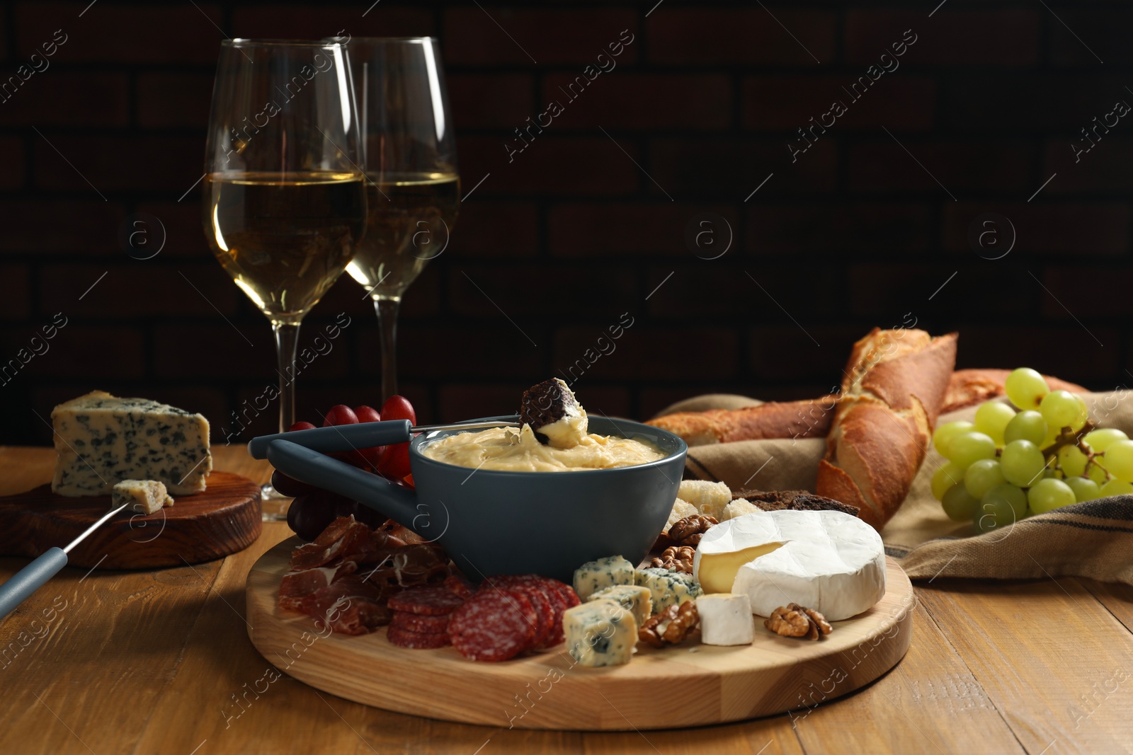 Photo of Fondue pot with tasty melted cheese, forks, different snacks and wine on wooden table