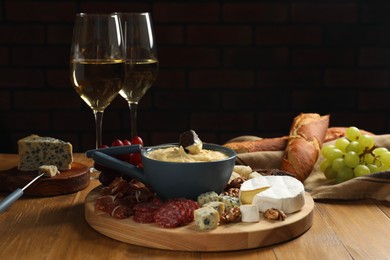 Fondue pot with tasty melted cheese, forks, different snacks and wine on wooden table